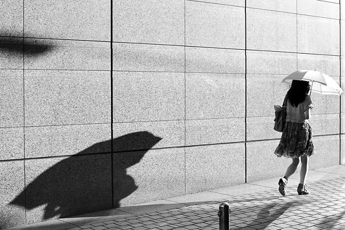 Woman walking with an umbrella casting a shadow on a tiled wall in a Japan street photography black and white shot.