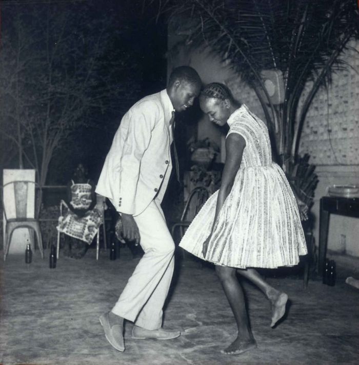 A black and white photo of a couple dancing joyfully at a party, wearing vintage attire, capturing a famous moment in history.