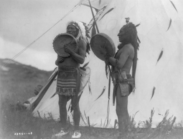 Two Dakota Men Playing Hand Drums Outside Of A Tipi, 1908