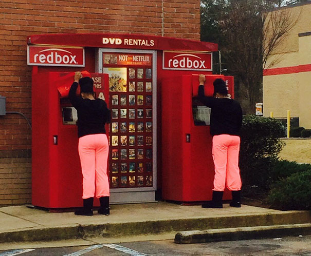 Two womans standing near redboxes and wearing same clothes