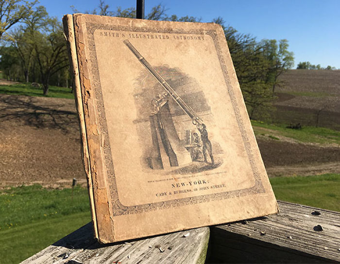 Old book titled "Smith's Illustrated Astronomy" found in a thrift store, displayed on a wooden railing outdoors.