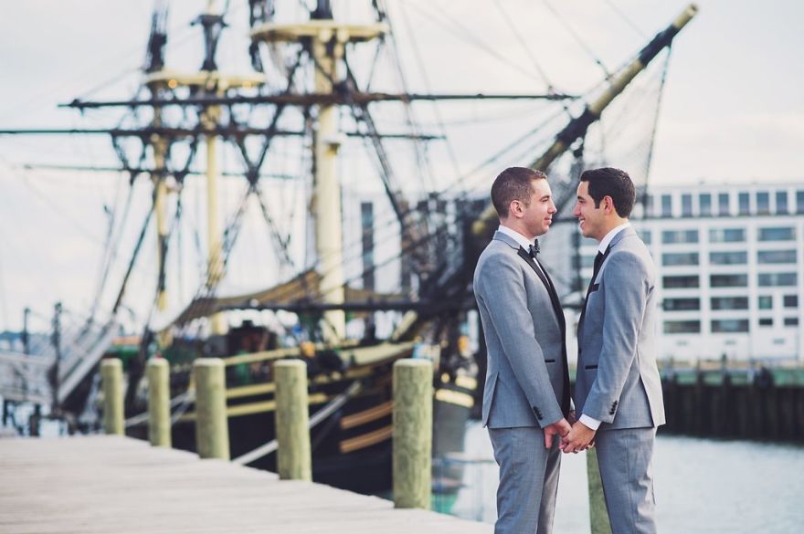 Two men holding hands and looking at each other near a ship 