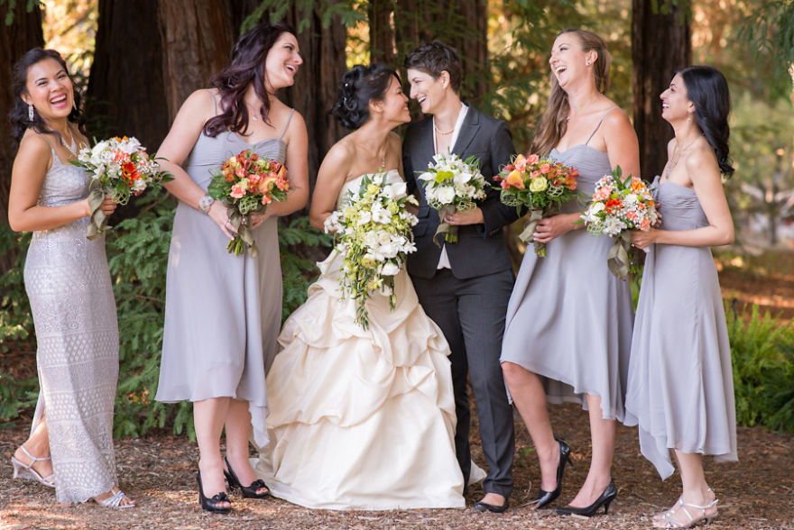 Tw women laughing and holding hands while grooms stand near by 