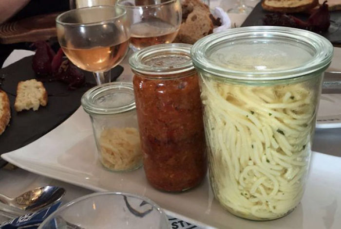 Spaghetti served in jars with wine glasses, showcasing restaurants going too far with unusual food presentation.