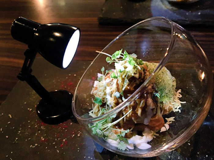 Creative restaurant food presentation in a tilted glass bowl illuminated by a mini spotlight.