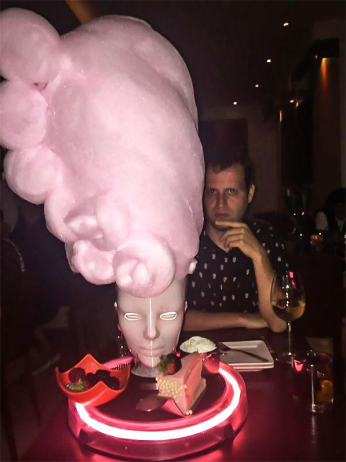 Restaurant serving with cotton candy on a mannequin head, extravagant presentation with a person in the background.