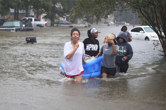 People Walk Down A Flooded Street As They Evacuate Their Homes After The Area Was Inundated With Flooding From Hurricane Harvey