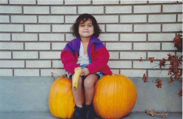 a girl sitting on the pumpkins holding a banana 