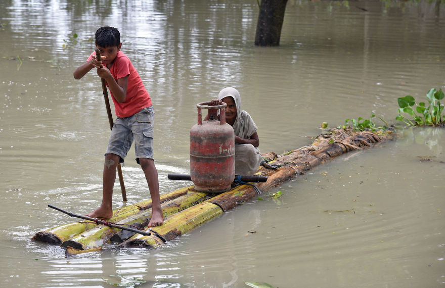 A Boy Rows A Makeshift Raft As He Transports A Woman And A Cooking Gas Cylinder Through The Flood Waters In Assam, India