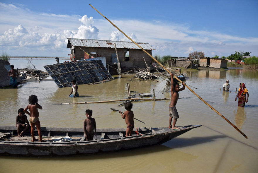 Children Row A Boat As They Pass Through Damaged Houses At A Flood-affected Village In Morigaon District In The Northeastern State Of Assam, India