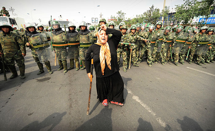 Chinese Riot Police Watch A Muslim Ethnic Uighur Woman Protest In Urumqi In China’s Far West Xinjiang Province Following A Third Day Of Unrest, 7 July 2009 