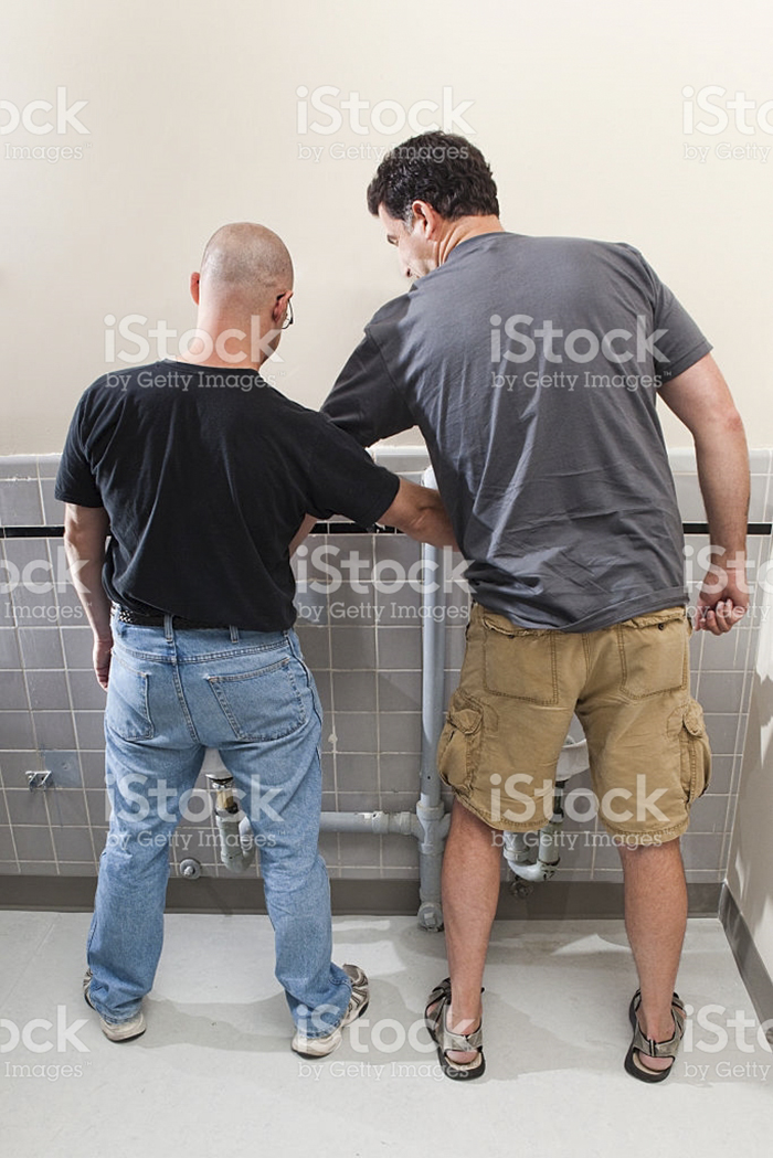 Two men helping each other to pee in toilet
