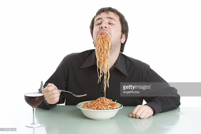 A man in a black shirt greedily eating spaghetti in ecstasy