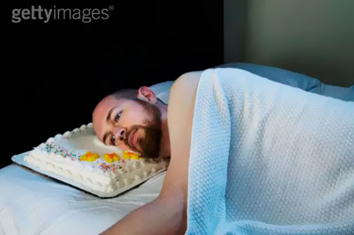 A man lying down in bed and a white cake instead of a pillow