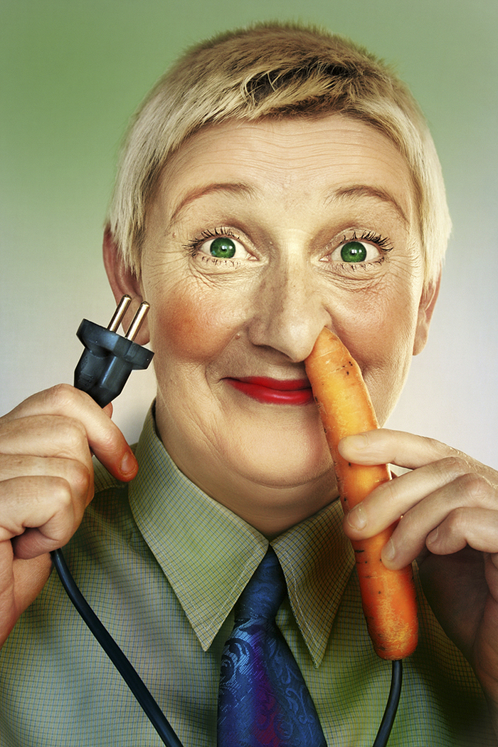 Happy short hair woman with green eyes putting an electric carrot into her nose and holding a power cord in other