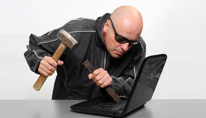 Bald man with sunglasses trying to break into laptop with chisel and hammer