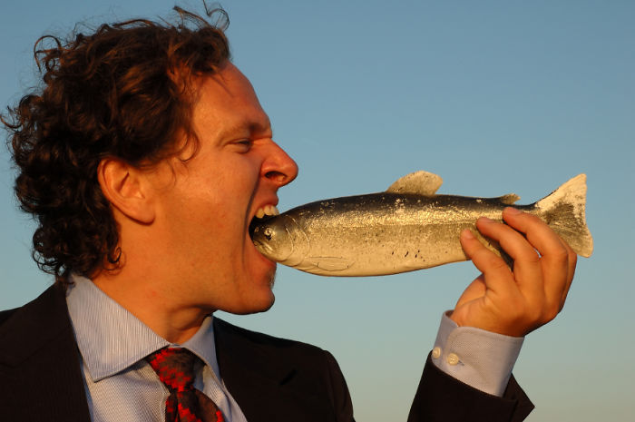 Man in a suit eating raw fish starting with a head