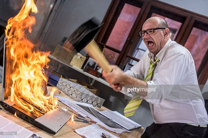 Angry man hitting burning laptop with a hammer