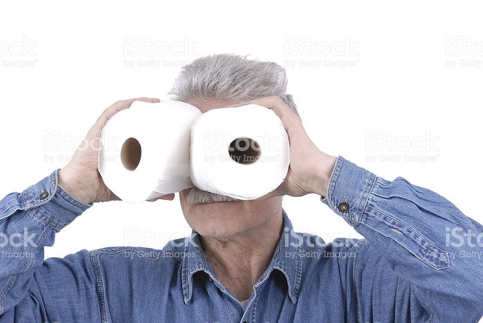 An elderly man in a denim shirt is looking through toilet paper rolls
