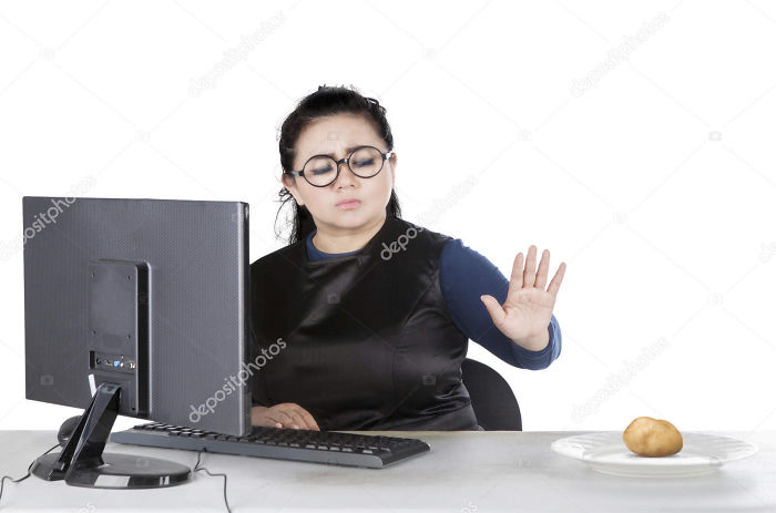 Woman is sitting next to a computer and refusing to eat a potato