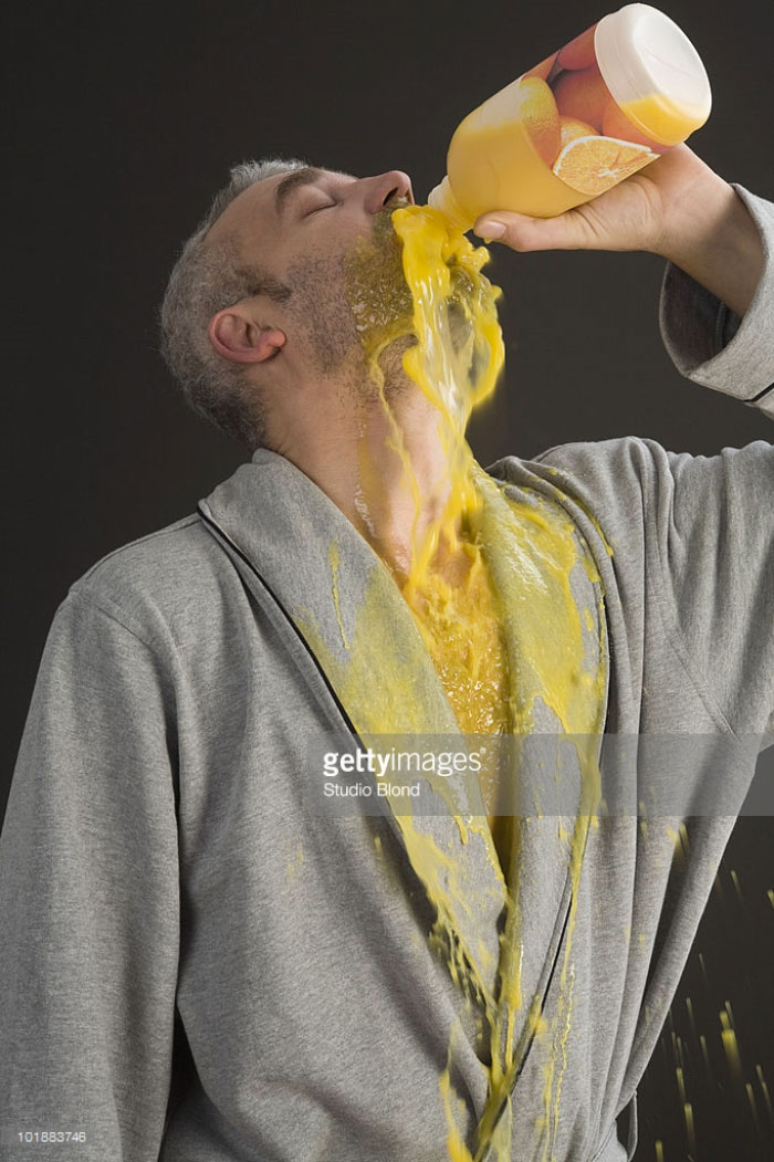 Man in a bathrobe pouring orange juice into his mouth and spilling it out on himself