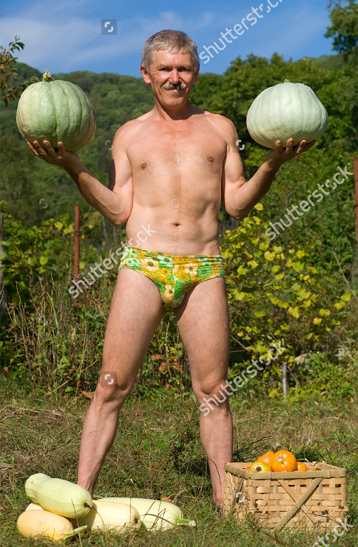 An elderly man stands naked in underwear and holds two gourds in his hands