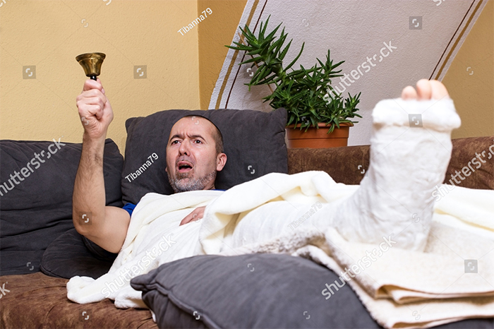 Man lying down in bed with broken leg and a bell in the right hand