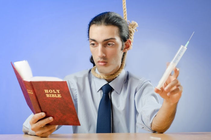 A young man with gallow rope on his neck the Holy Bible in his right hand and a syringe in his left hand