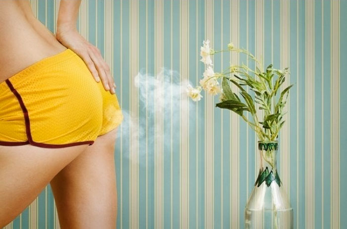 Butt in yellow shorts letting the gass out on a vase with flowers and wallpaper with stripes in the background