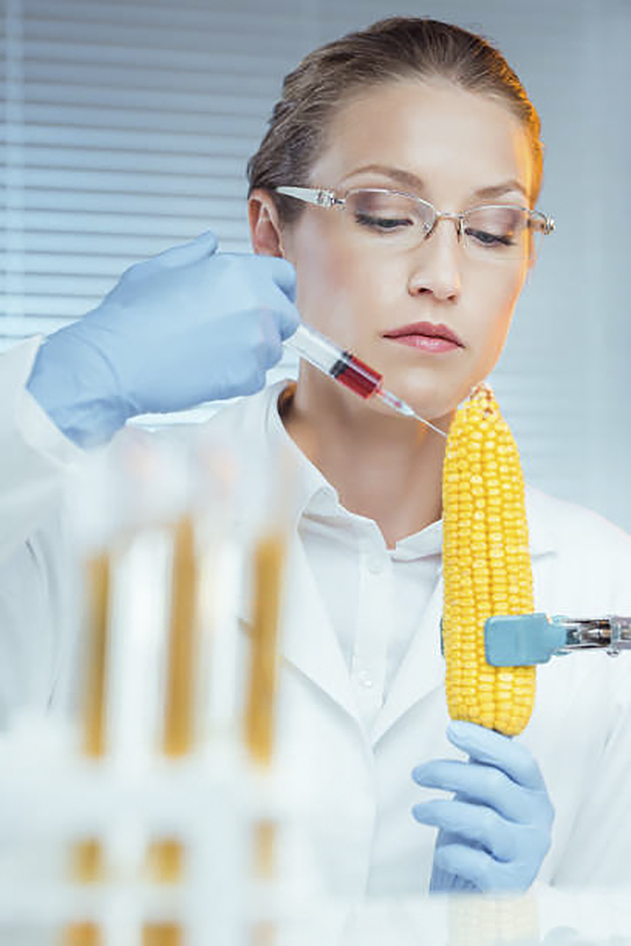 Woman with a serious face injecting red liquid into corn