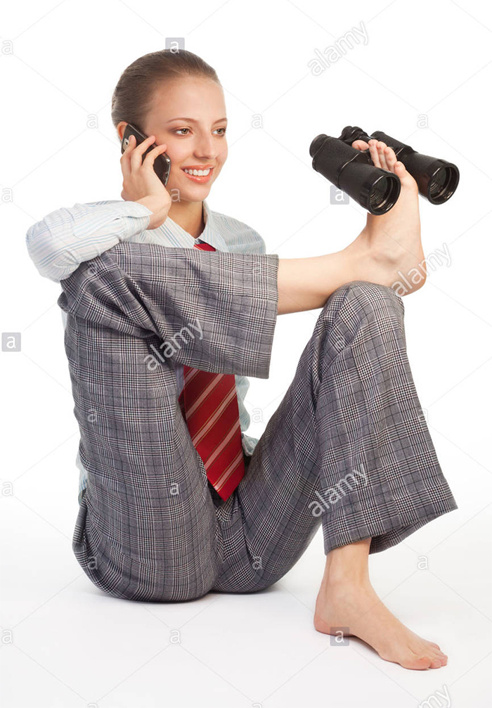A woman in a classy outfit is on the phone and holding binoculars with her foot