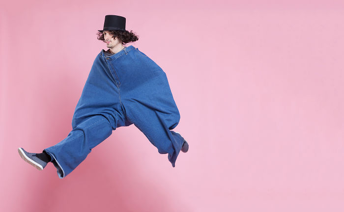 A man jumped into the air with a large blue jeans in front of a pink background