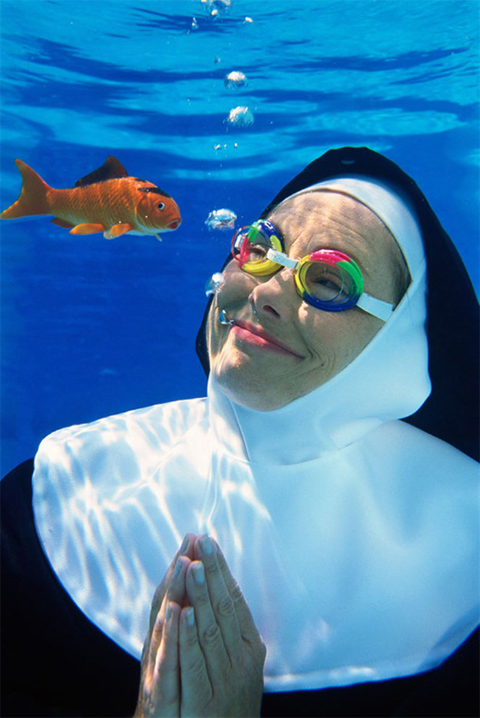 Smiling nun with swimming glasses underwater praying and goldfish swimming