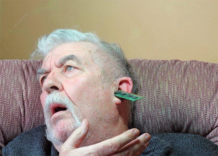 An elderly man with his mouth open sitting on soft furniture and a circuit board in his ear