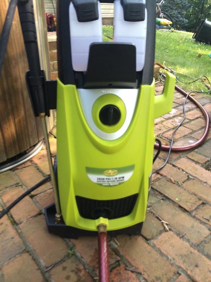 A pressure washer resembling a robot, resembling accidental cosplay, stands on a brick path outdoors.