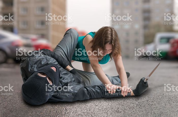 A woman tackling a mugger with a knife in his hands by pressing him on the ground