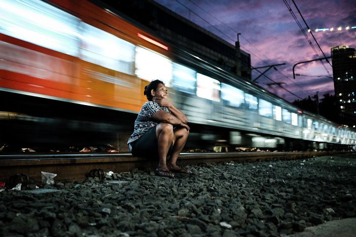 Una mujer está sentada cómodamente en las vías del tren mientras éste pasa a un par de metros detrás de ella