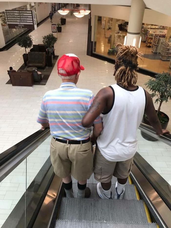 Young Man Helping An Older Man Down An Escalator
