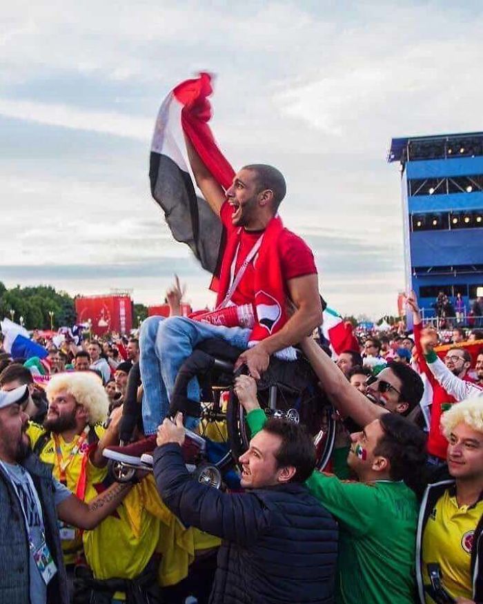 Hincha egipcio siendo levantado por hinchas mexicanos y colombianos para que pueda ver jugar a su equipo
