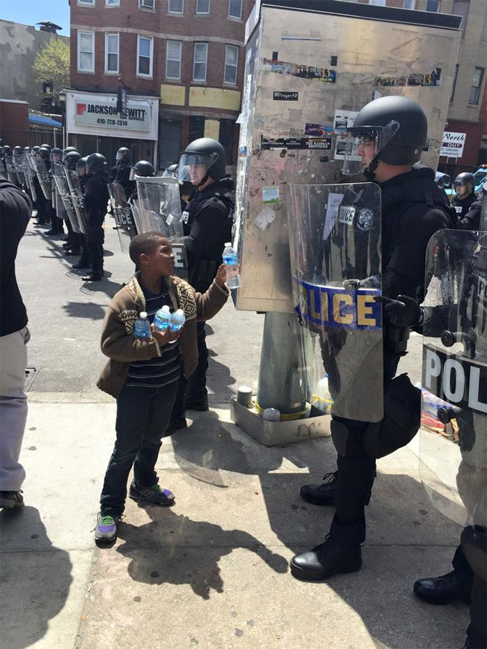 Niño ofreciendo agua a un policía durante una manifestación en Baltimore