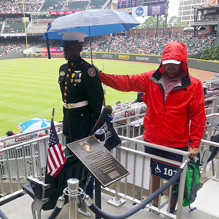 Fan del béisbol sosteniendo un paraguas sobre un miembro de las Fuerzas JROTC en el Día de los Caidos