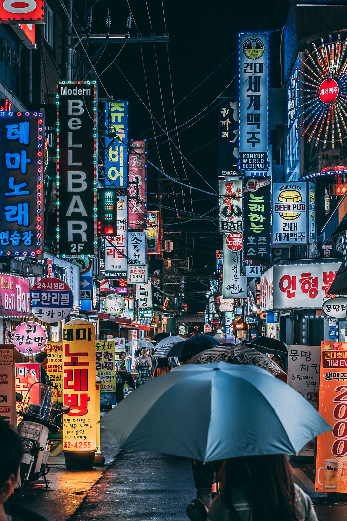 Night street scene in Seoul filled with colorful neon signs and people walking under umbrellas in the rain.