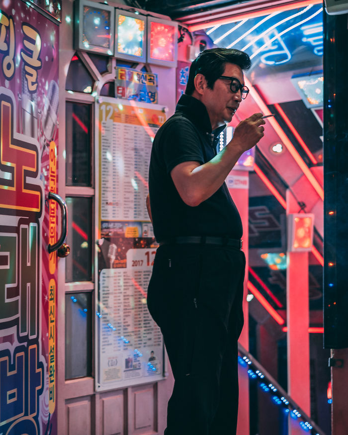 Man standing outside a neon-lit karaoke bar in Seoul, captured in vibrant street photography by an English teacher.