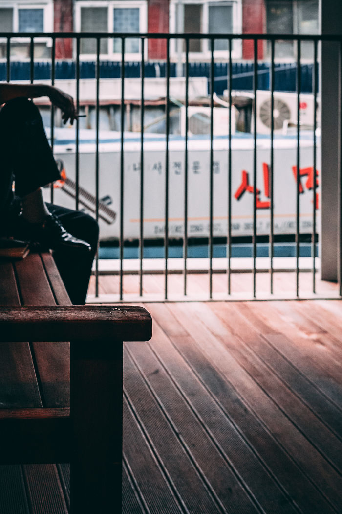 Person sitting on wooden bench near a railing in Seoul, capturing moments as an English teacher living abroad.