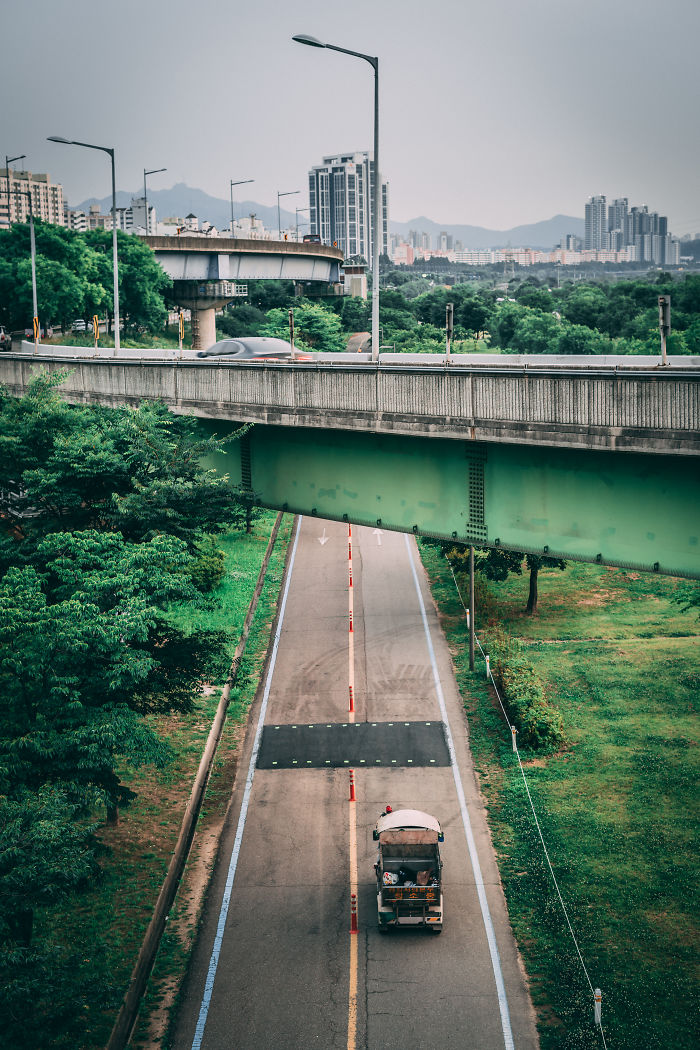 Urban road scene in Seoul with greenery, a vehicle, and city buildings in the background, showcasing life in Seoul.