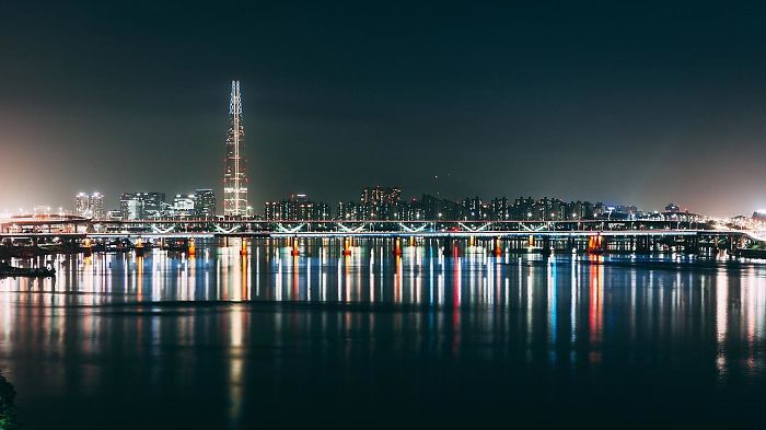 Night view of Seoul cityscape with illuminated skyscraper and bridge reflecting on the calm river, showcasing life as an English teacher.