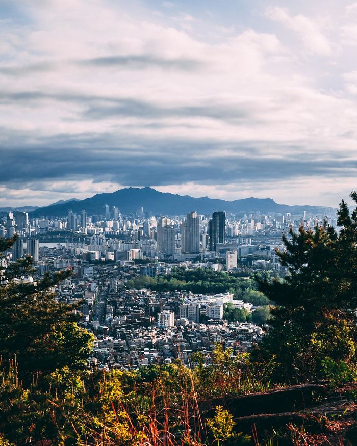 Seoul cityscape from a hillside with urban buildings, mountains in the background, and cloudy sky highlighting English teacher life.
