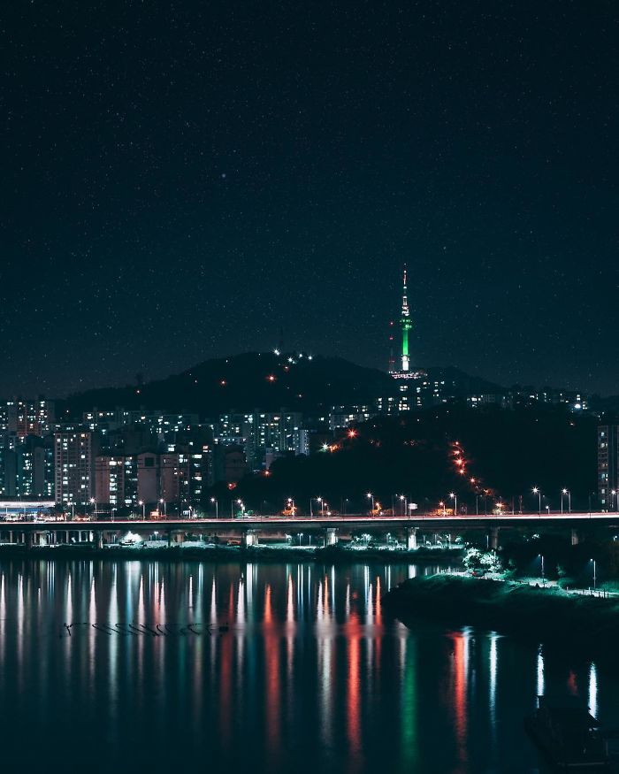 Night skyline of Seoul with Namsan Tower lit green, city buildings, and reflections on the river, showcasing life as an English teacher.