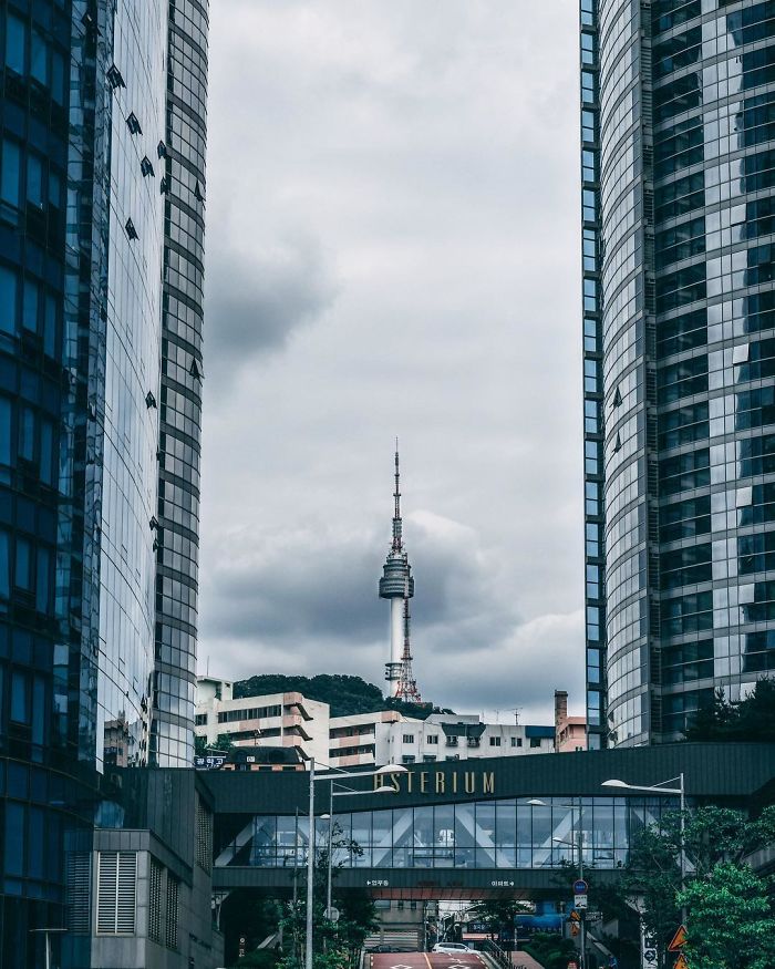 View of Seoul cityscape with modern buildings and the Namsan Seoul Tower under a cloudy sky.