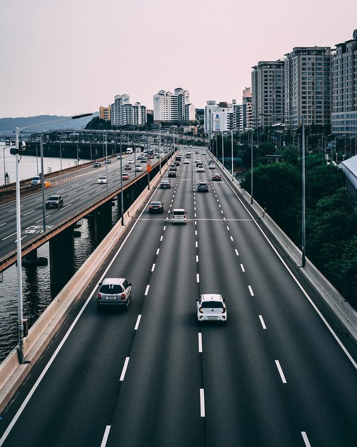Wide view of Seoul highway with cars driving alongside the river and tall apartment buildings in the background.